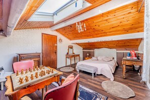 Une chambre avec un plafond en bois, un lit, un bureau avec un jeu d’échecs et une chaise rouge.