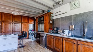 Una cocina con armarios de madera, lavavajillas de acero inoxidable, un lavabo y un reloj en la pared.