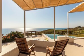 Une terrasse avec deux chaises en bois, une petite piscine et une vue sur la mer.
