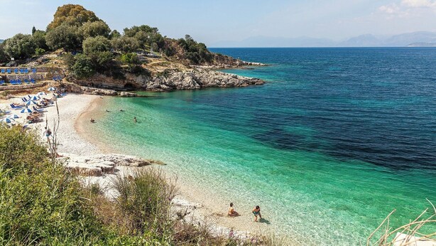 A beach with clear turquoise water, a rocky outcrop with trees, and a row of beach umbrellas. - Josephine House - Four Bedroom Villa, Sleeps 8 (Kalami)