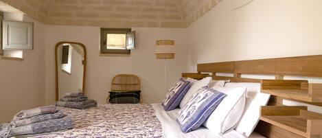 Un dormitorio con una cama, cabecera de madera, un espejo, una ventana y un estante fijado a la pared.