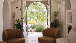 An interior view with an open doorway leading to a garden, two armchairs, and a bookshelf. - Trullo Terra Dolce - Four Bedroom Villa, Sleeps 8 (Ostuni)
