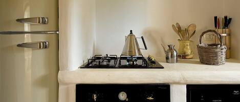 Une cuisine équipée d’une cuisinière à gaz, d’une cafetière, d’une bouilloire et d’un panier posé sur le comptoir.