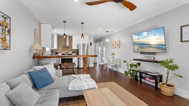 Ein modernes Wohnzimmer mit einem grauen Sofa, einem Holztisch und einem Fernseher, der eine Strandansicht zeigt.