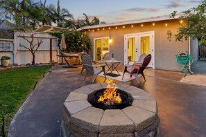 Ein Garten mit Feuerstelle, Gartenmöbeln und einem Haus mit Schiebetür.