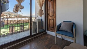 A balcony with a view of a green sports field, a wooden door, and a blue chair.