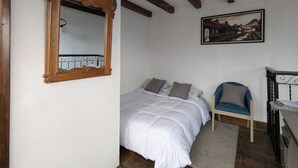 A bedroom with a large mirror, a bed with white bedding, a chair, a painting on the wall, and a ceiling fan.