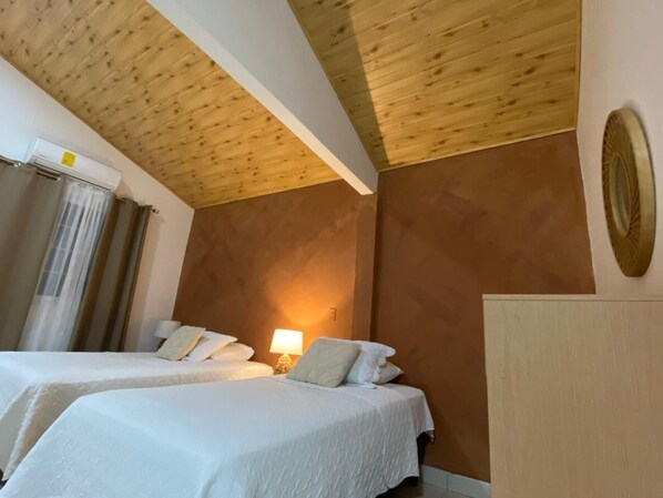 A hotel room with two beds, wooden ceiling, and a wall-mounted lamp. - zenda house (Hicaco)