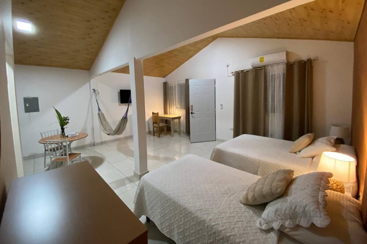 A hotel room with two beds, a dining table, a hammock, and a small kitchen area.