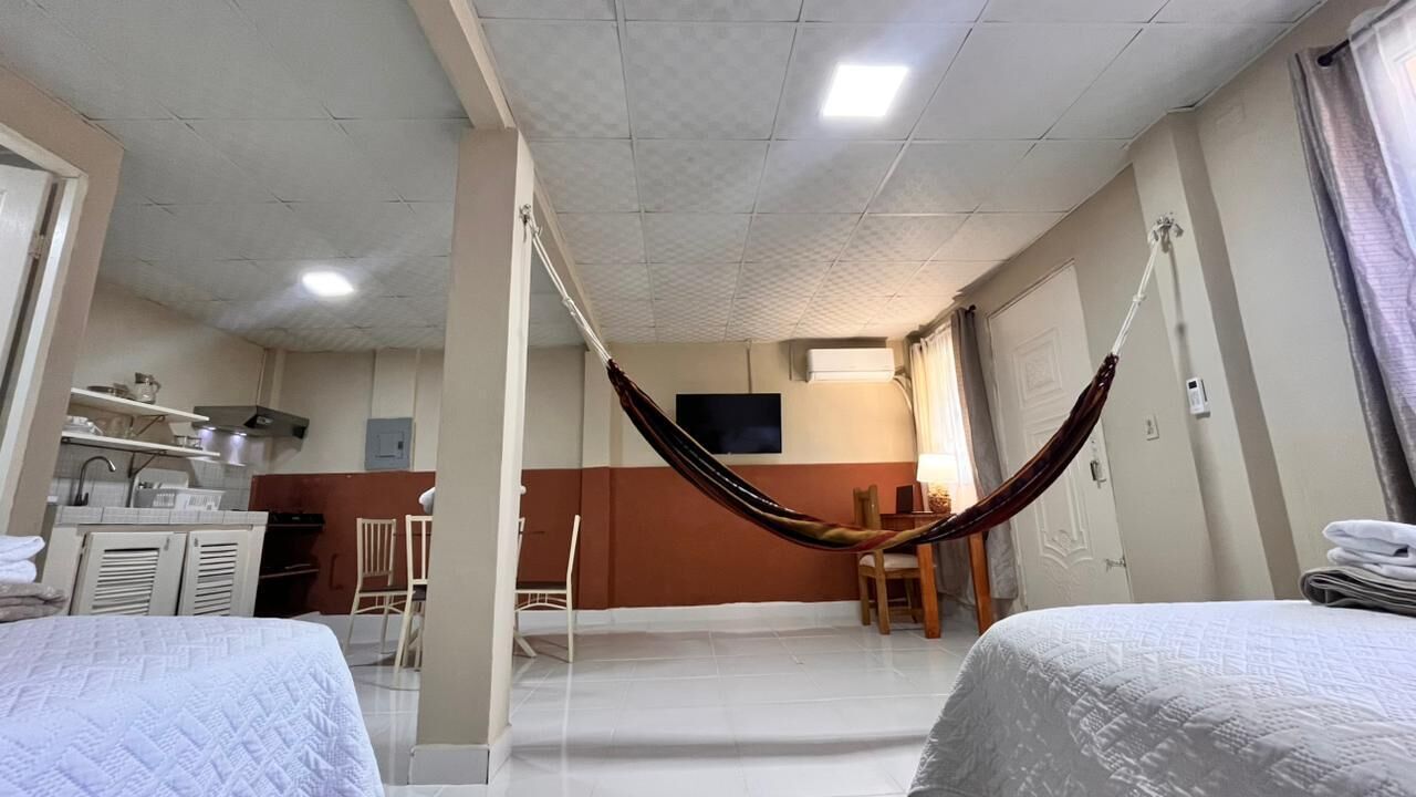 Habitación de hotel con dos camas, una hamaca, kitchenette y televisor.
