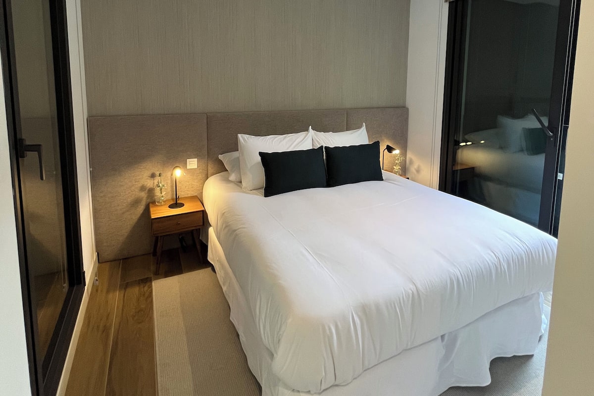 Una moderna camera d'hotel con un letto grande, un comodino con una lampada e vista sulla città da una grande finestra.