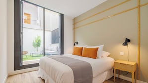 A bedroom with a large bed, a nightstand, a lamp, and a sliding glass door leading to a balcony with a plant. - Santa Lucía by Wynwood House (Madrid)