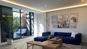 A modern living room with a blue sofa, a wooden coffee table, and a large window with a view of the outdoors. - Santa Lucía by Wynwood House (Madrid)