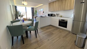 A modern kitchen with white cabinets, a stainless steel refrigerator, and a dining area with a round table and chairs. - Santa Lucía by Wynwood House (Madrid)
