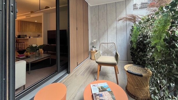 A modern living room with a large sliding glass door leading to a kitchen, a wicker chair, and a small table with a magazine. - Santa Lucía by Wynwood House (Madrid)