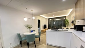 A modern kitchen with a central island, a dining area with a round table and chairs, and a large window providing natural light. - Santa Lucía by Wynwood House (Madrid)