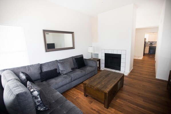 A modern living room with a grey sectional sofa, a wooden coffee table, a fireplace, and a hallway leading to a kitchen. - Charming 2-bedroom condo with fitness room and AC in marvelous Tucson (Tucson)