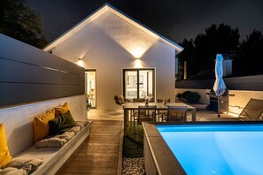 Une maison moderne dotée d’une piscine, d’un espace salon extérieur et d’un coin barbecue.