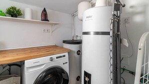 Een kleine wasruimte met een Samsung wasmachine, een Haier droger en een klein plankje met een plant en een decoratief object.