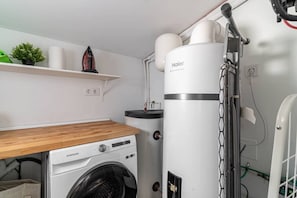 Une petite buanderie équipée d’un lave-linge Samsung, d’un sèche-linge Haier et d’une petite étagère agrémentée d’une plante et d’un objet décoratif.