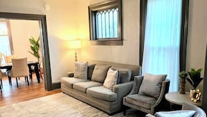 Una sala de estar con un conjunto de sofá, un sillón redondo, piso de madera y un área de comedor al fondo.