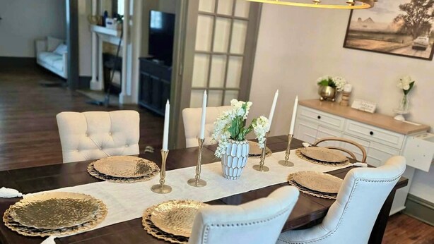 Un comedor con una mesa de madera oscura, sillas tapizadas en blanco y una araña con múltiples velas.