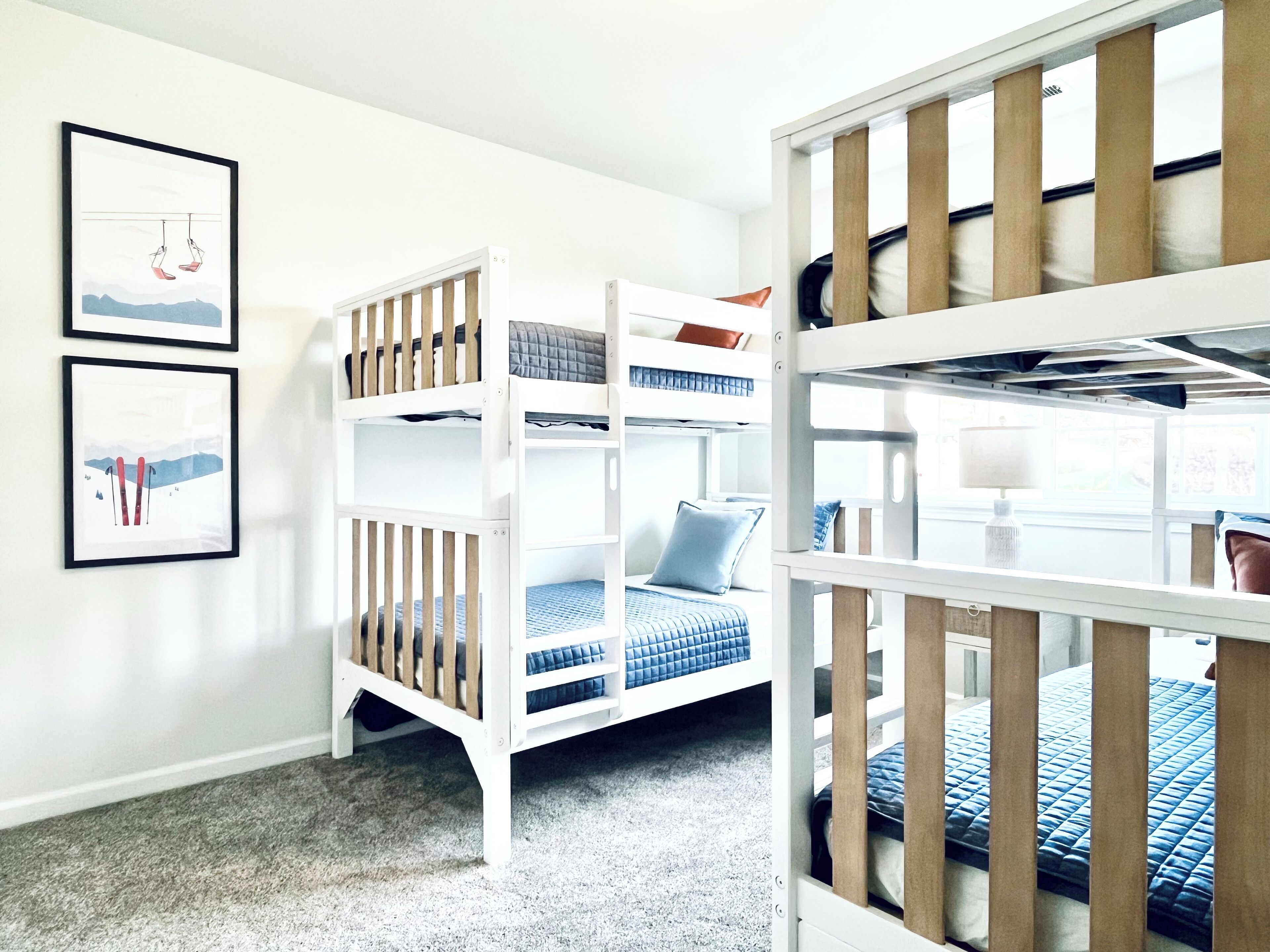 A bunk bed room with a white and blue color scheme, a framed picture on the wall, and a window with natural light.