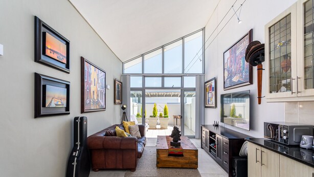 Un salon moderne avec un canapé, une table basse et une guitare appuyée contre le mur. Des tableaux encadrés ornent le mur, et une grande fenêtre offre une vue sur l’extérieur.