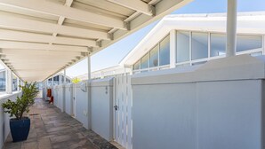 Un couloir couvert, doté d’un sol en pierre, de murs blancs et d’une fenêtre en verre sur le côté droit.