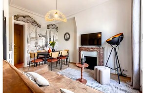Ein modernes Wohnzimmer mit Sofa, Couchtisch, Esstisch und Stühlen. Es gibt einen Kamin, einen Fernseher und eine Satellitenschüssel.