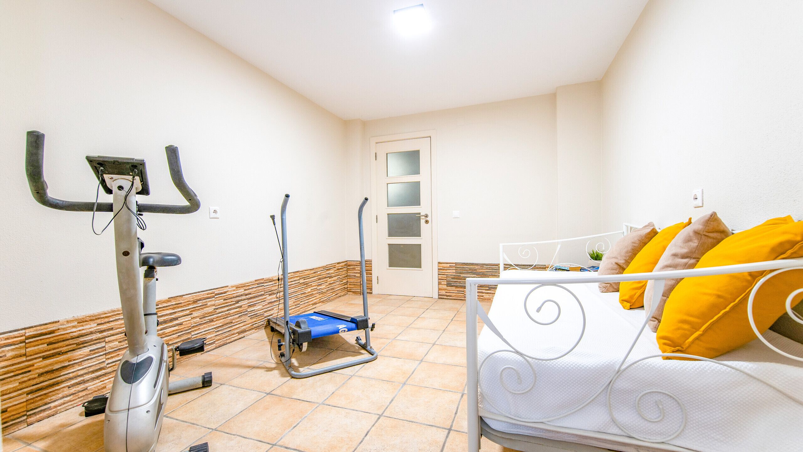A bedroom with a bed, exercise equipment, and a door.