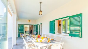 A dining area with a long table, white chairs, and a view of the outdoors. - Villa w/ Heatable Pool and BBQ in Albufeira (Albufeira)