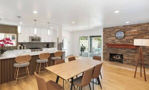 A modern kitchen with white cabinets, a central island with bar stools, and a dining area with a wooden table and chairs. - Spacious 6-bedroom house with fitness room and AC in charming Buena Park (Buena Park)