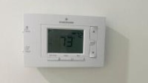 Een digitale thermostaat aan een muur, waarop een temperatuur van 73 graden staat aangegeven.