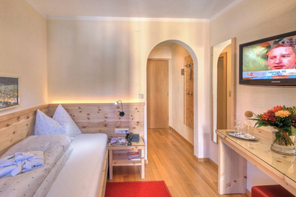 A hotel room with a bed, a desk with a TV, a wooden headboard, and a painting on the wall.