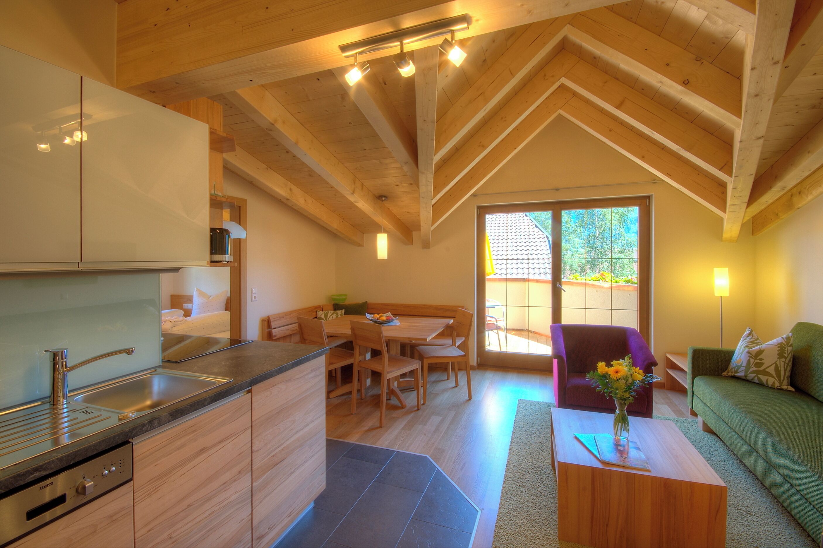 Una cocina moderna con armarios de madera, una zona de comedor con mesa y sillas, un sofá y una mesa baja con un jarrón.
