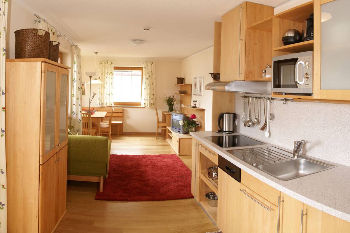 A compact kitchen with wooden cabinets, a microwave, a sink, and a dining area with a table and chairs.