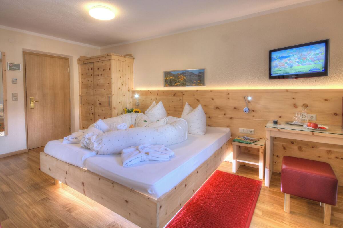 A hotel room with a wooden bed, a desk, a television, and a red rug.