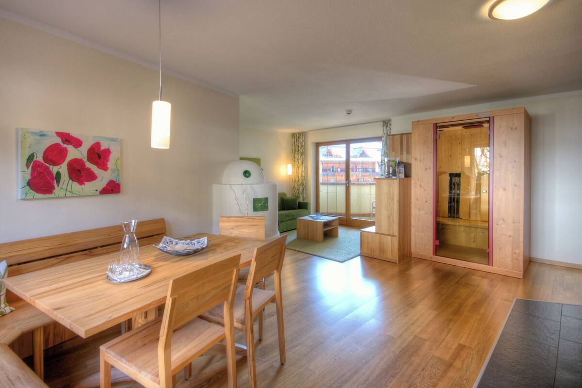 A dining area with a wooden table, chairs, and a bench. There is a painting on the wall and a lamp above the table.
