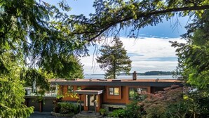 Une maison moderne avec une façade en pierre, un jardin bien entretenu et une vue sur l’eau.