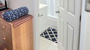 Ein Zimmer mit einem Holzschrank, einem gemusterten Teppich, einem Traumfänger an der Wand und einer weißen Tür, die ins Bad mit einer Duschvorhang führt.