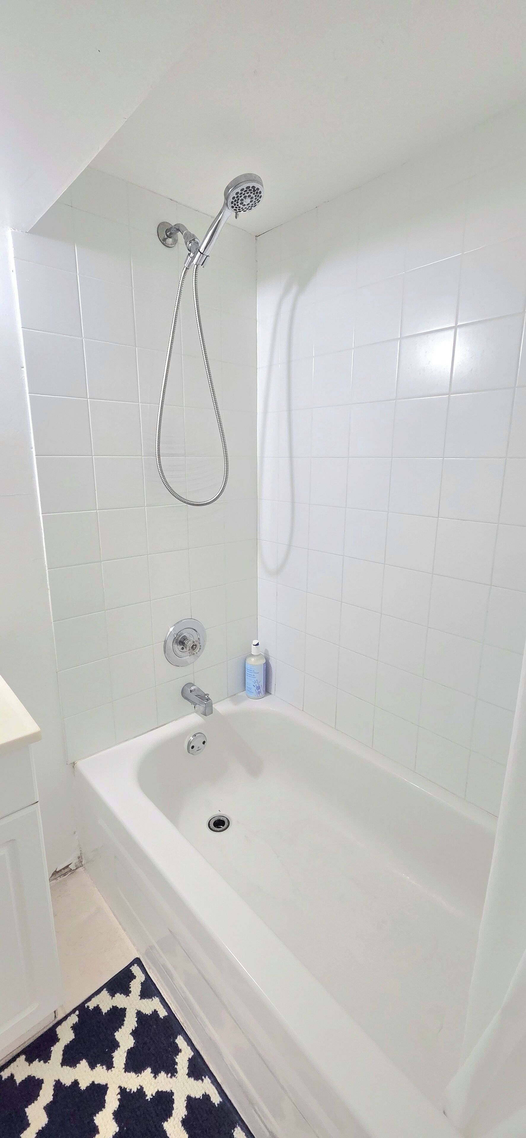 A bathroom with a white bathtub, a showerhead, and a hand soap dispenser.