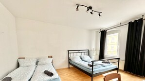 A room with two beds, a wooden chair, a table, and a window with curtains. - Modern apartment for sale in Chemnitz (Chemnitz)