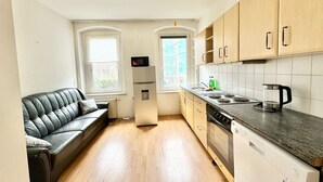 A compact kitchen with a black leather sofa, wooden cabinets, a microwave, and a coffee maker. - Modern apartment for sale in Chemnitz (Chemnitz)