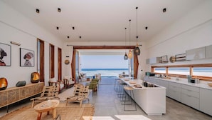Una cucina moderna con vista sull'oceano, dotata di isola centrale, sgabelli da bar e zona pranzo anch'essa con vista.