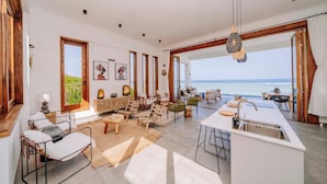 Un'ampia zona giorno con una grande finestra vista mare, un'isola nella cucina e un angolo salotto con vista.