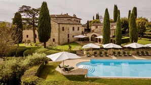 Un espace piscine agrémenté de chaises longues et de parasols, entouré de jardins bien entretenus et de grands cyprès.