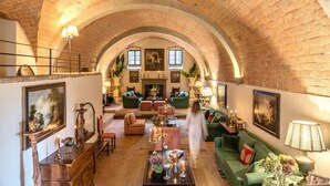 Un vaste salon doté d’un haut plafond voûté en briques, de canapés verts, d’une cheminée et d’un escalier menant à un niveau supérieur.