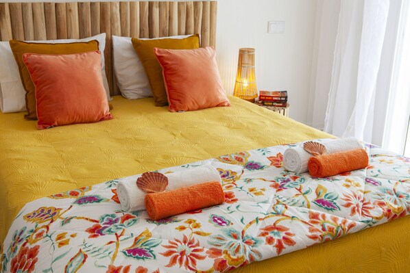A bed with a yellow bedspread, multiple pillows, and a floral-patterned blanket.