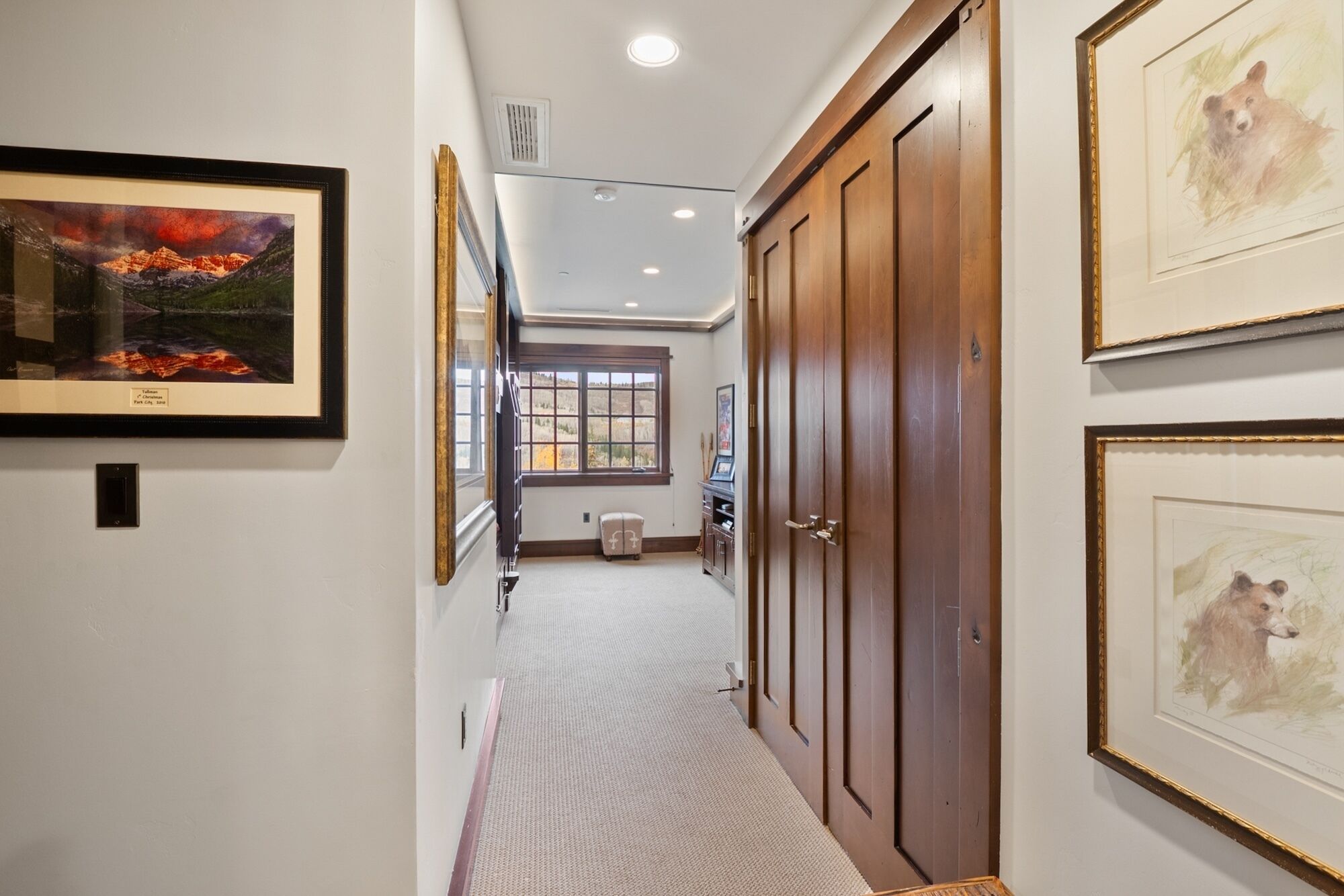 A hallway with framed artwork, a wooden door, and a window with a view of a landscape.